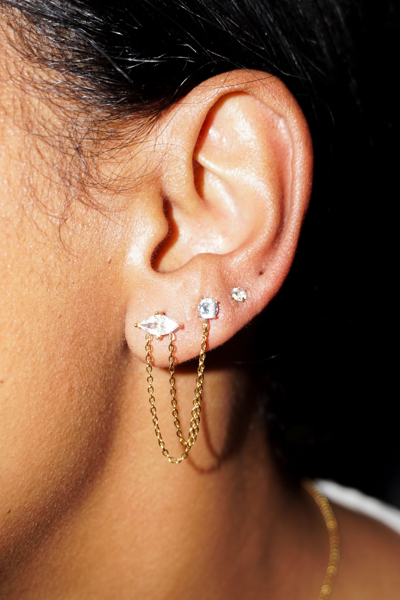 Close-up of an ear wearing gold hoop earrings with small gemstones against a dark background
