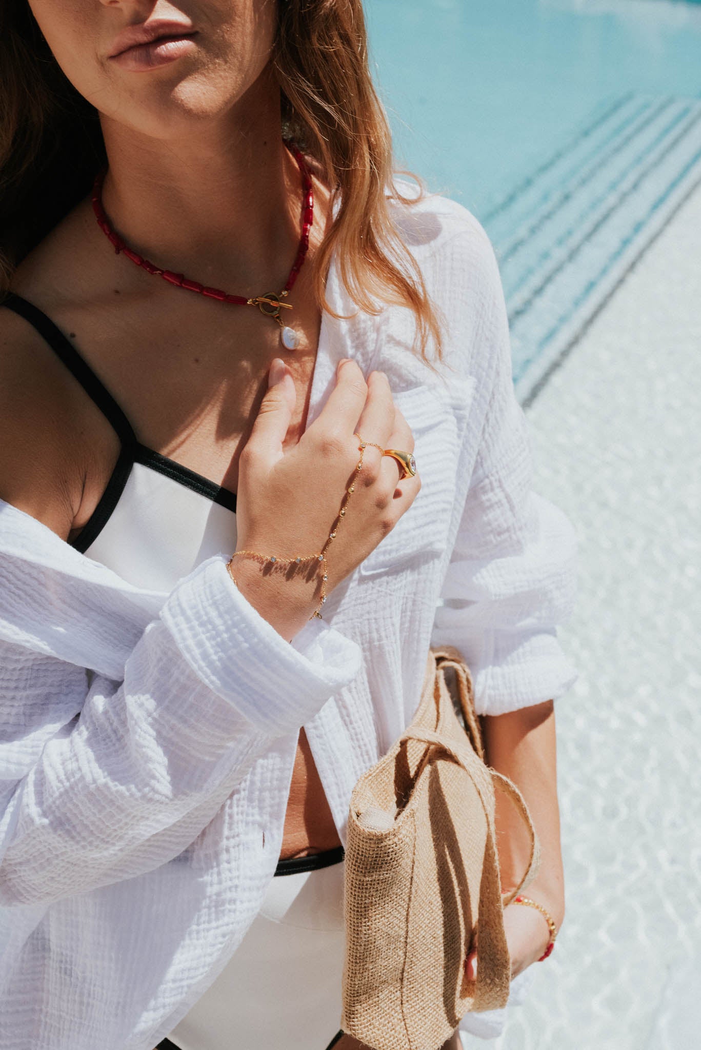 Woman wearing a white outfit with a black top, holding a straw bag, against a blurred outdoor background.