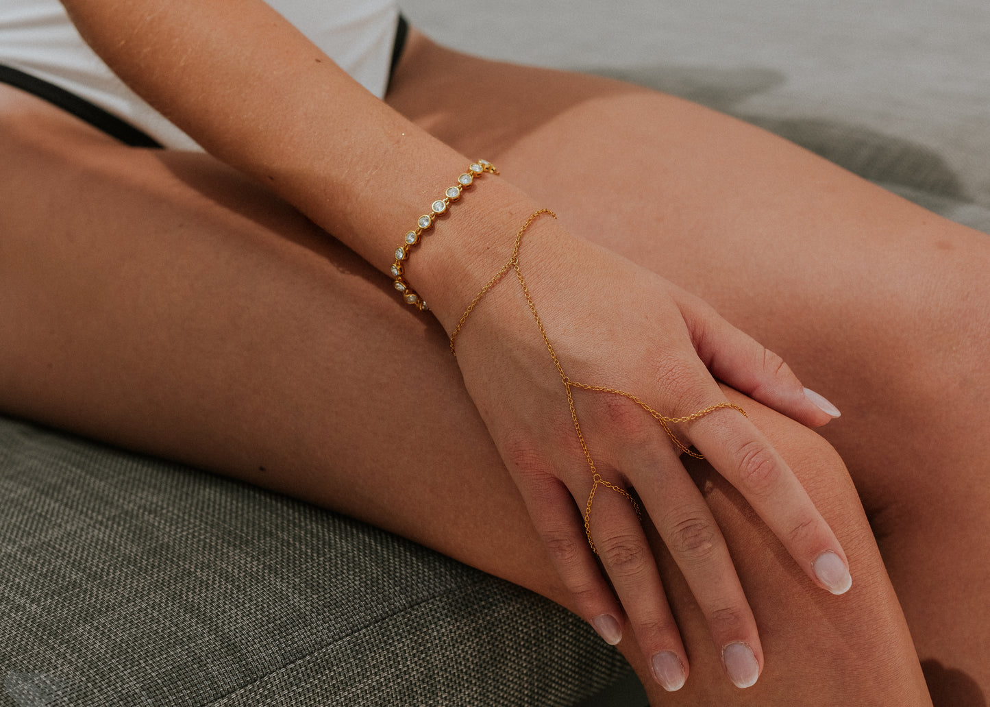 Close-up of a person's hand wearing gold jewelry on a neutral background