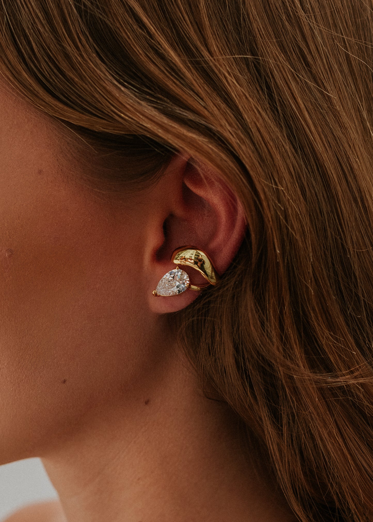 Close-up of a person wearing gold earrings with a blurred background