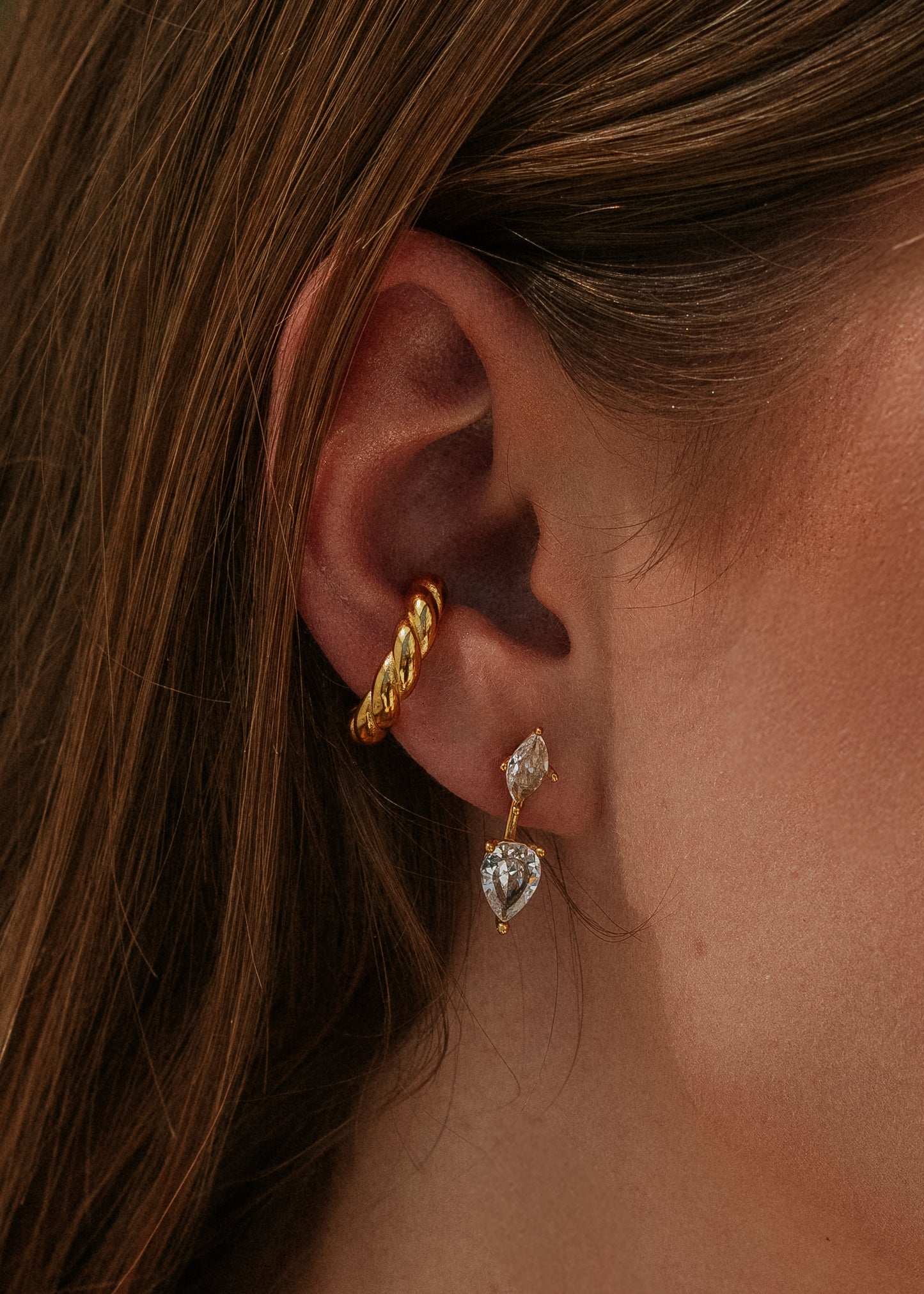 Close-up of an ear wearing gold hoop and diamond-shaped earrings.