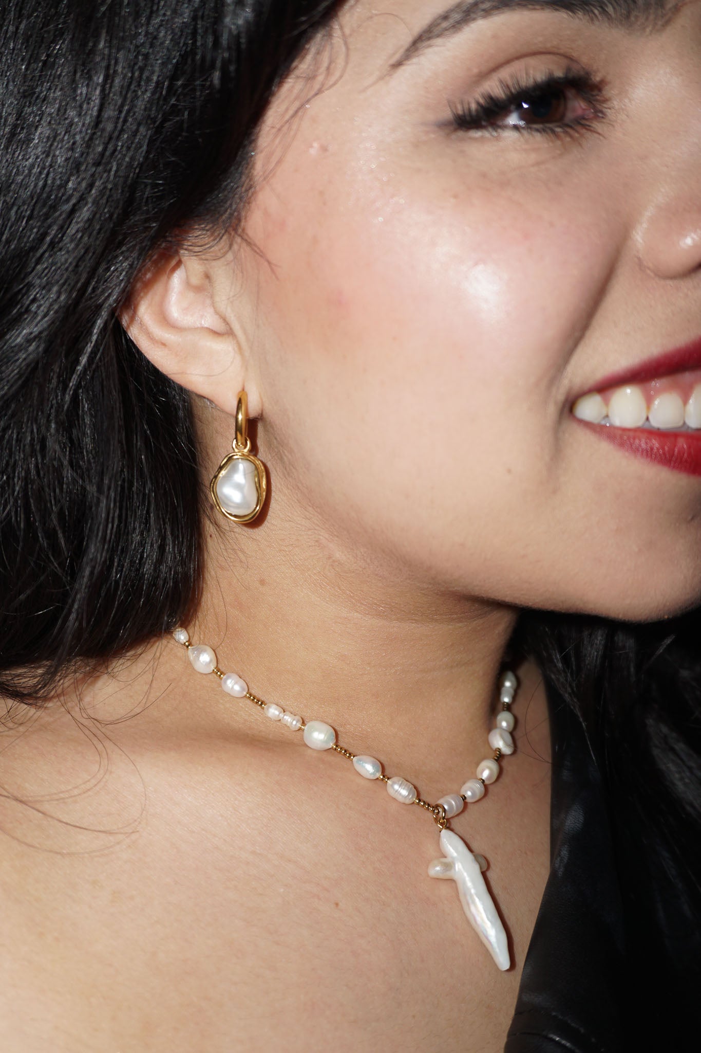 Close-up of a woman wearing pearl earrings and a necklace with a white pendant.