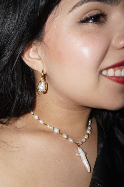 Close-up of a woman wearing pearl earrings and a necklace with a white pendant.