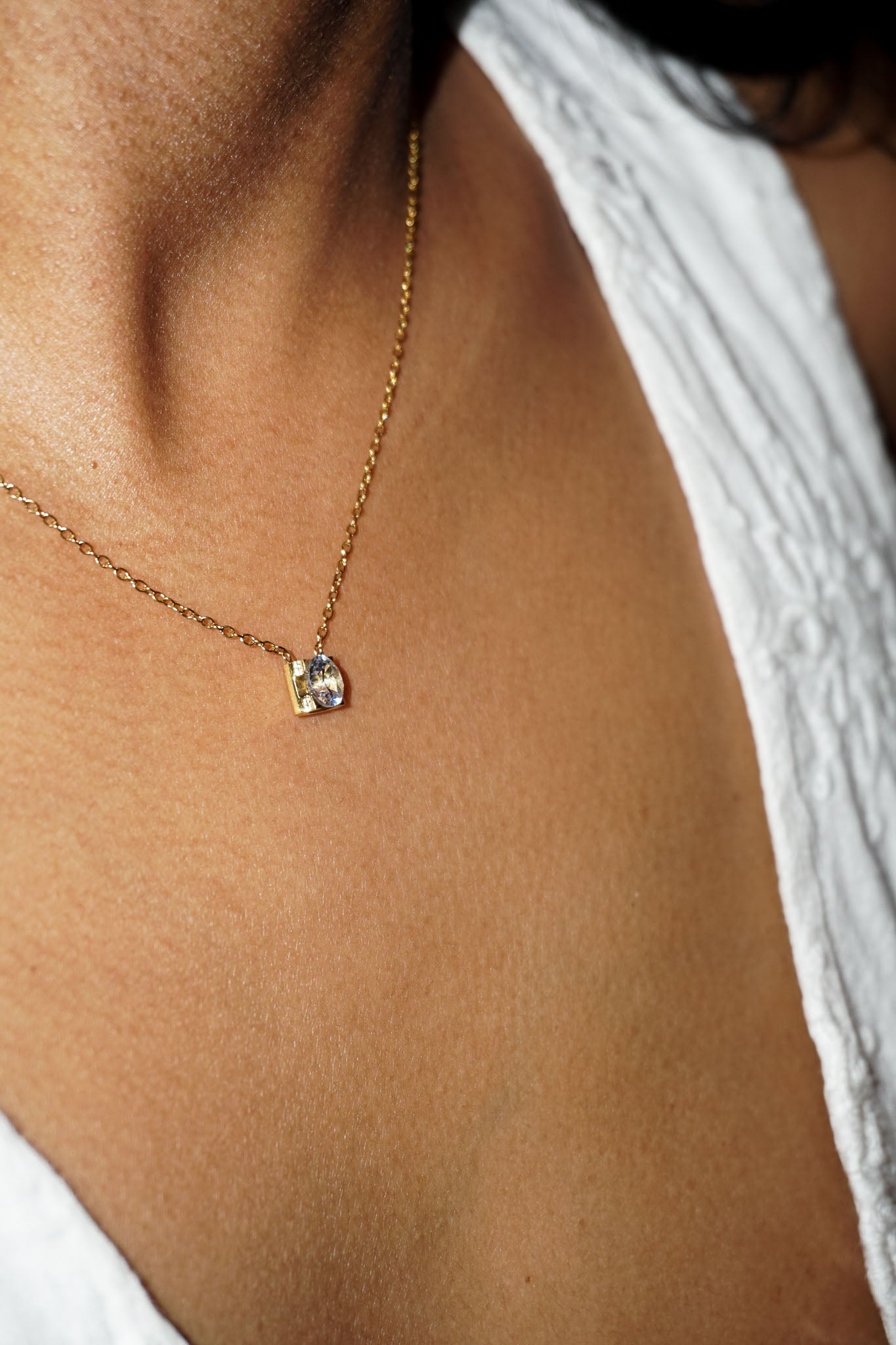 Gold necklace with a small pendant on a person wearing a white top.