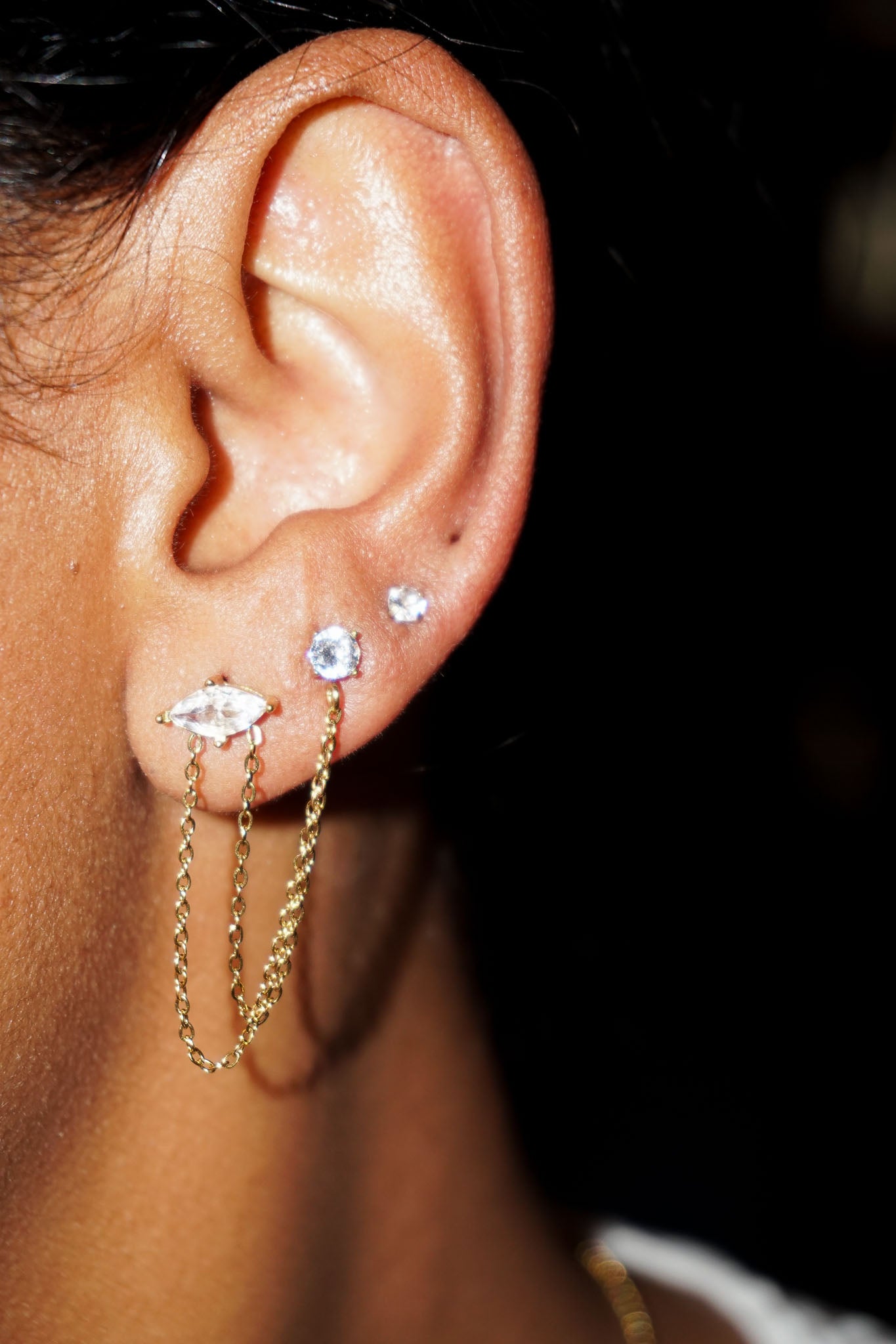 Close-up of an ear with gold earrings and gemstones against a dark background