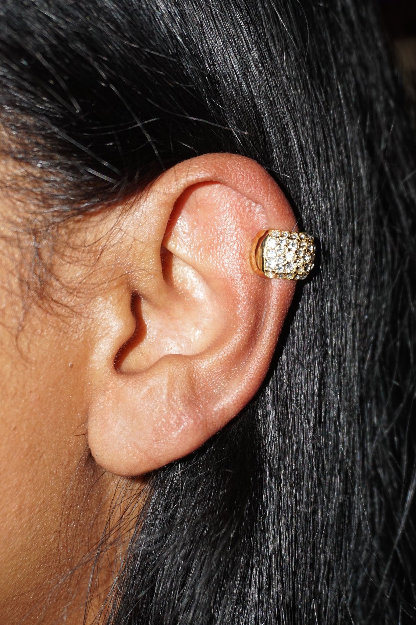 Gold cuff with embedded stones pavé diamonds close up on an ear