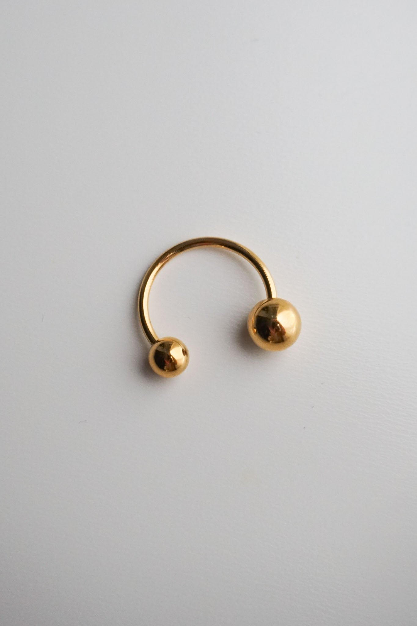 Gold hoop earring with spherical ends on a light gray background