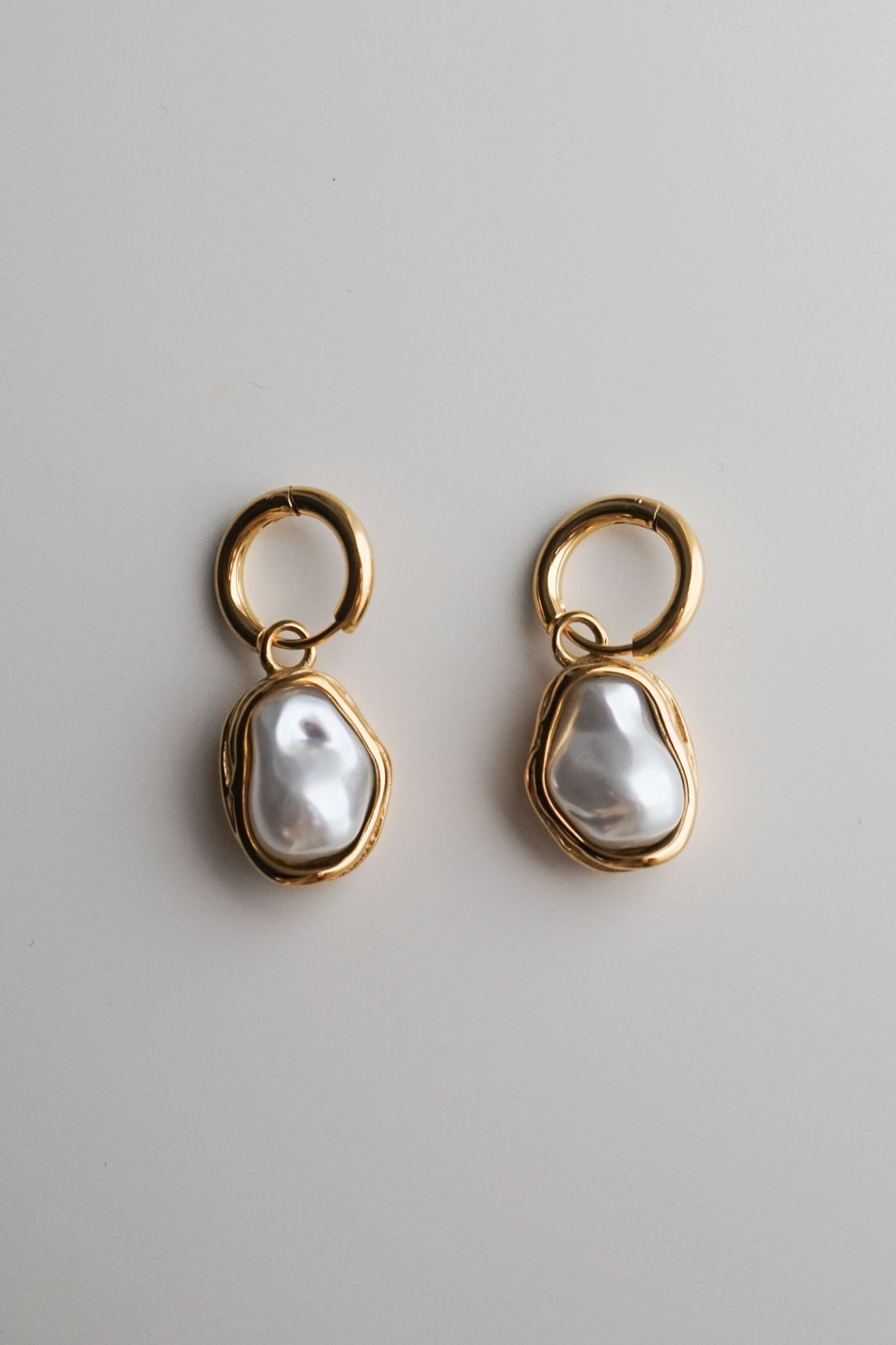 Pair of gold earrings with pearl-like stones on a light gray background