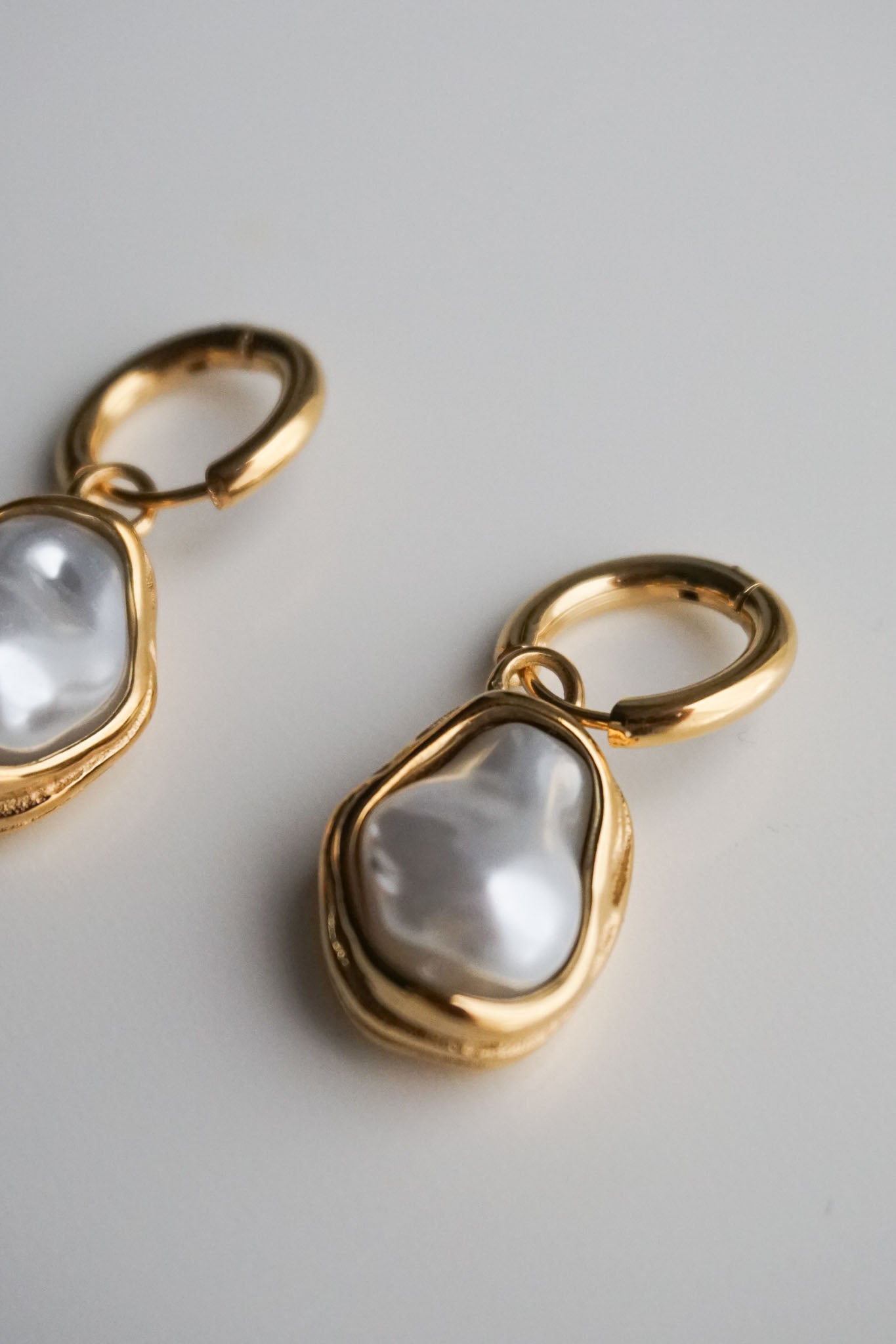 Gold earrings with pearl-like stones on a light gray background