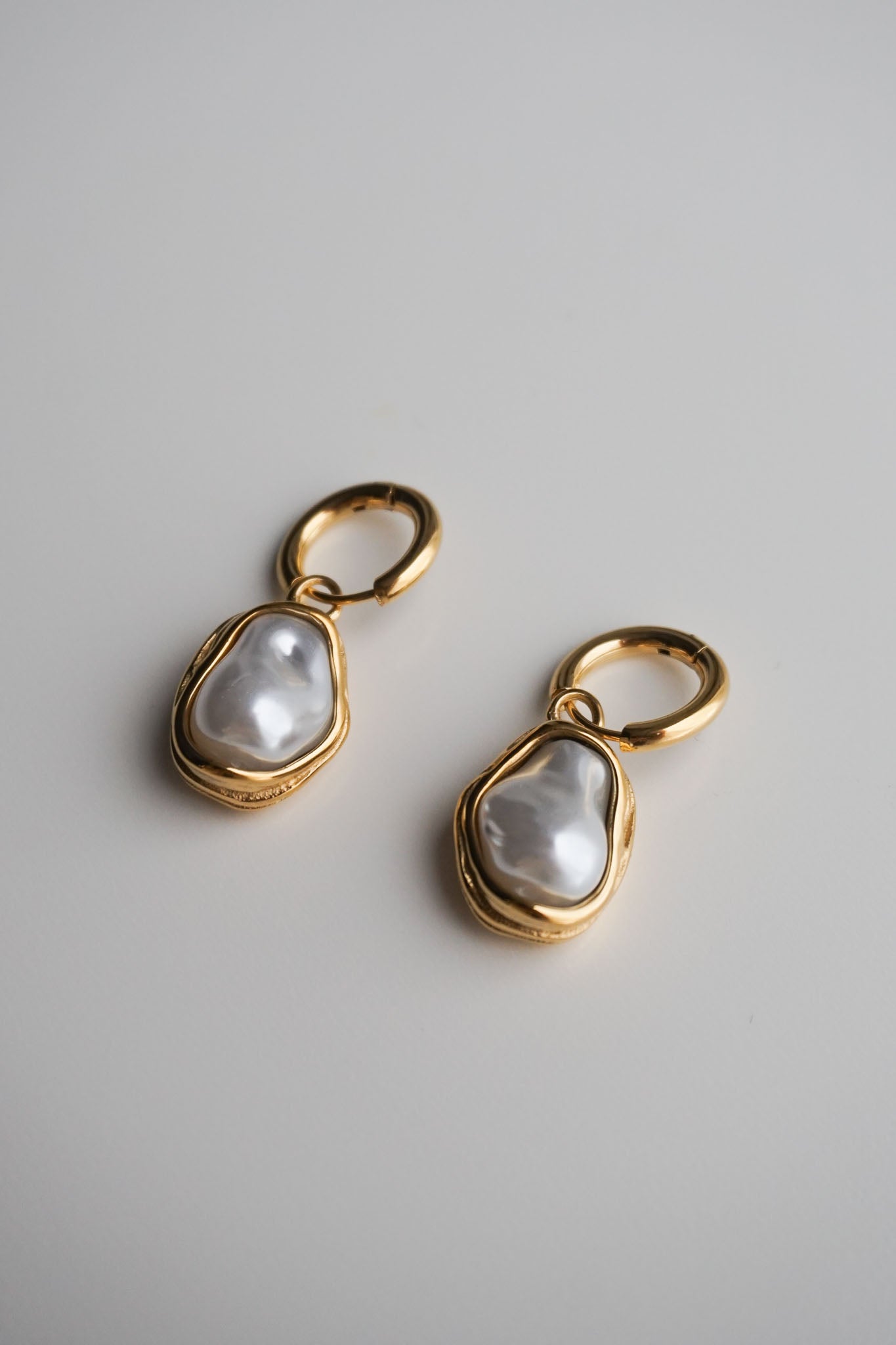 Gold earrings with pearl-like stones on a light gray background