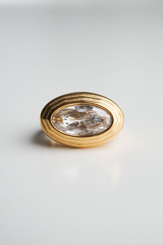 Gold ring with a clear gemstone on a light gray background