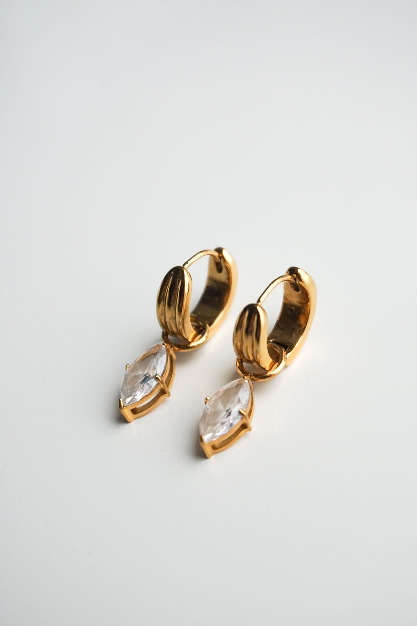 Gold hoop earrings with clear gemstones on a light gray background