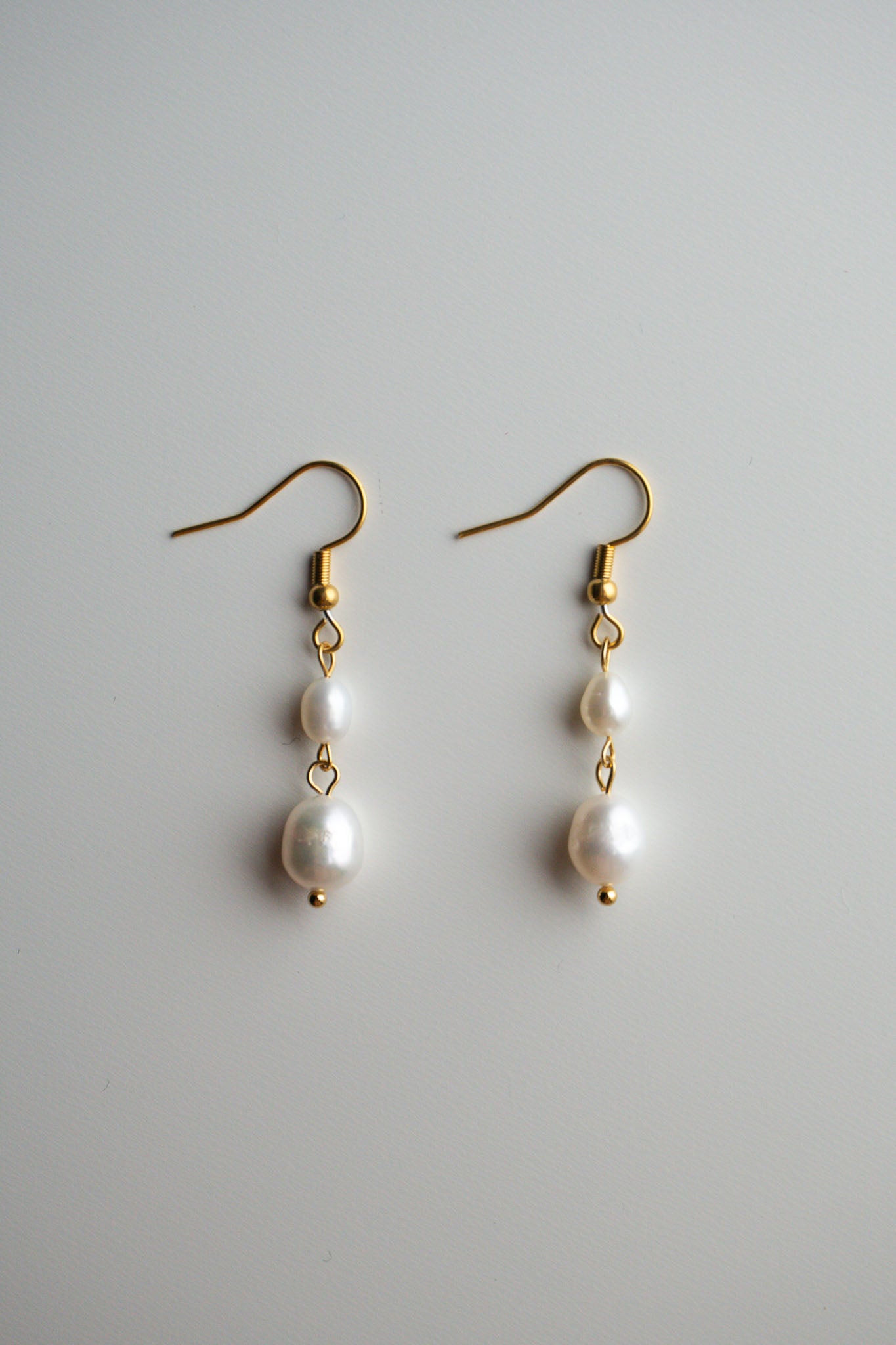A pair of gold dangle earrings with three white freshwater pearls of varying sizes