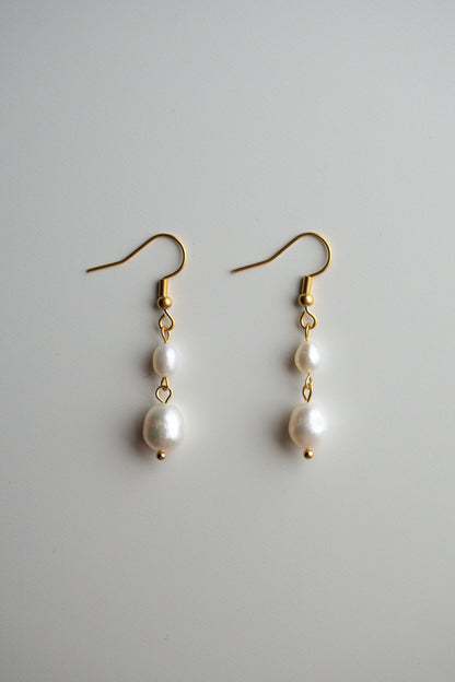 A pair of gold dangle earrings with three white freshwater pearls of varying sizes
