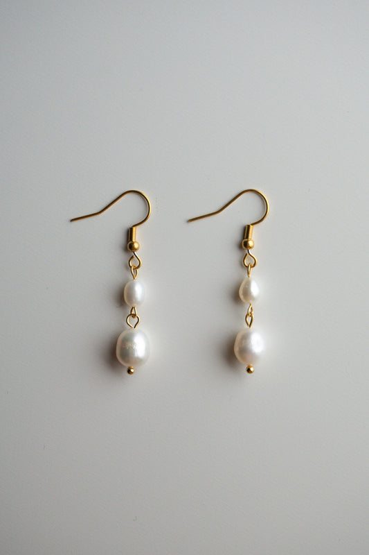 A pair of gold dangle earrings with three white freshwater pearls of varying sizes