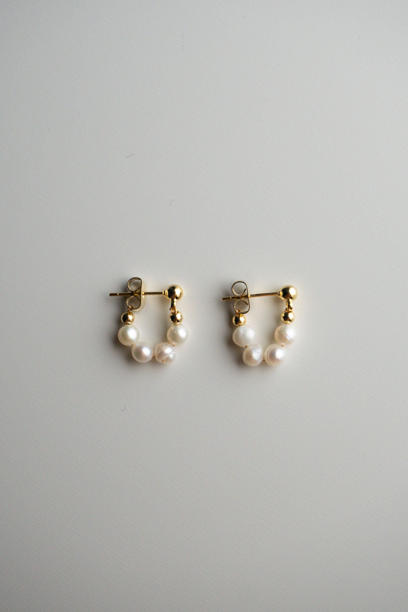A pair of gold hoop earrings with small pearl clusters at the bottom.