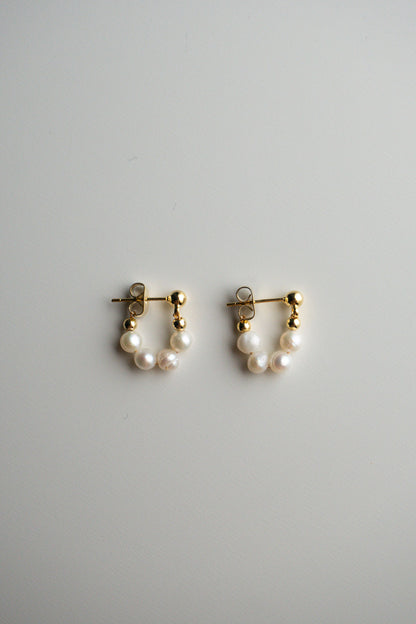 A pair of gold hoop earrings with small pearl clusters at the bottom.