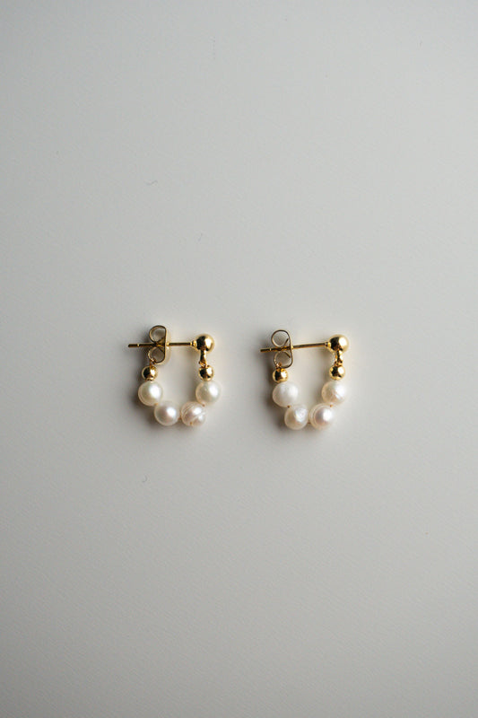 A pair of gold hoop earrings with small pearl clusters at the bottom.