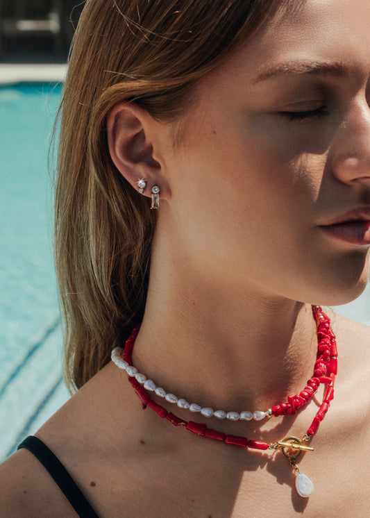Close-up of a woman wearing a red beaded necklace and earrings by a pool.