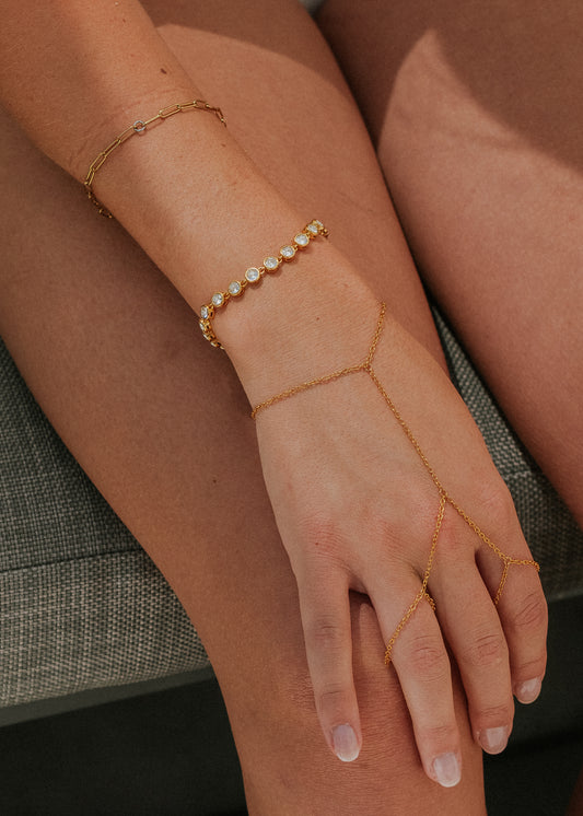 Gold anklets on a person's ankle and foot against a neutral background