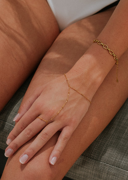 Gold hand chain worn on a wrist with a neutral background